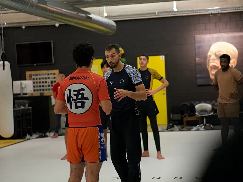 Een instructeur demonstreert clinch-technieken met een student in een MMA/grappling trainingsgroep.
