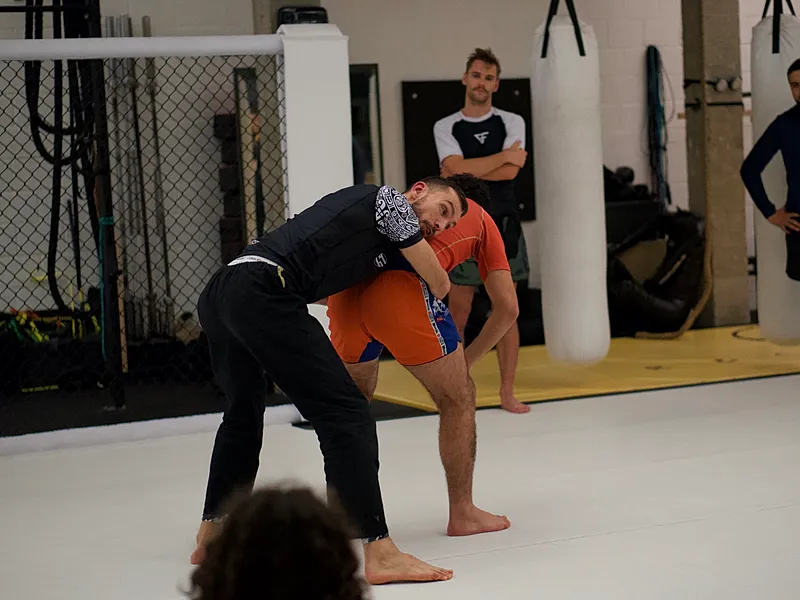 BJJ-beoefenaars demonstreren een grappling positie op de mat tijdens een groepsles in de gymzaal.