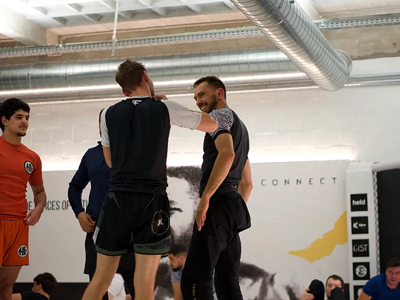 Instructeur demonstreert grappling-technieken met student terwijl andere deelnemers toekijken in een BJJ-trainingsgroep.
