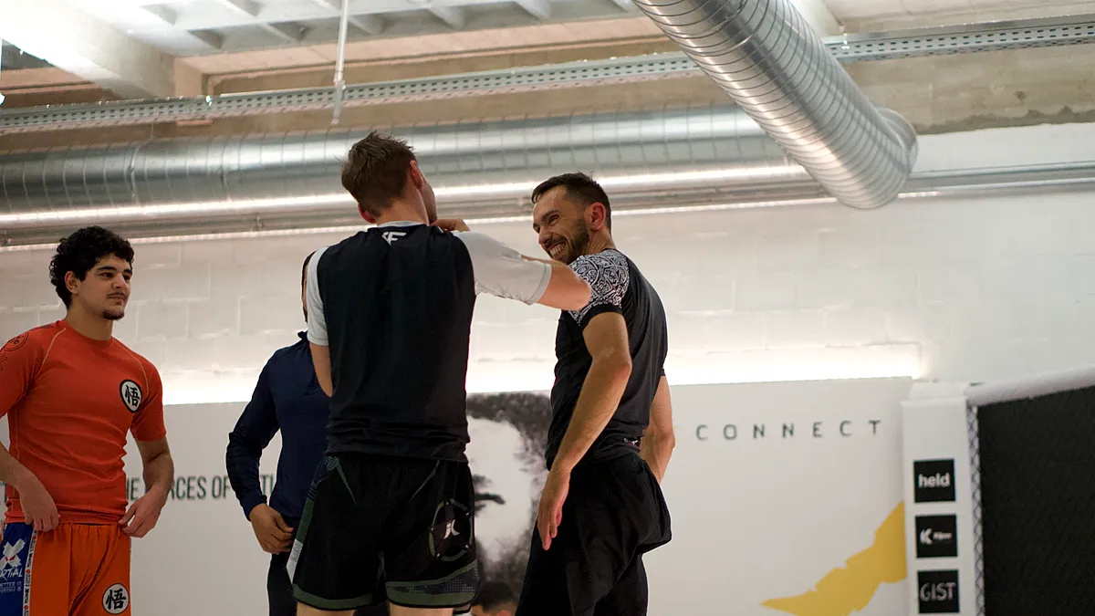 Instructeur demonstreert grappling-technieken met student terwijl andere deelnemers toekijken in een BJJ-trainingsgroep.