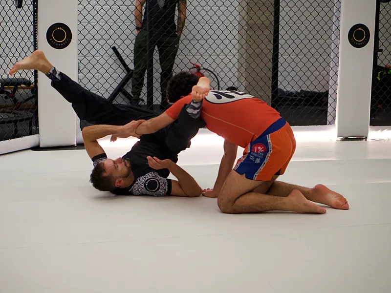 Twee BJJ-beoefenaars trainen op de mat waarbij één fighter in guard positie ligt en de ander een sweep-beweging uitvoert.