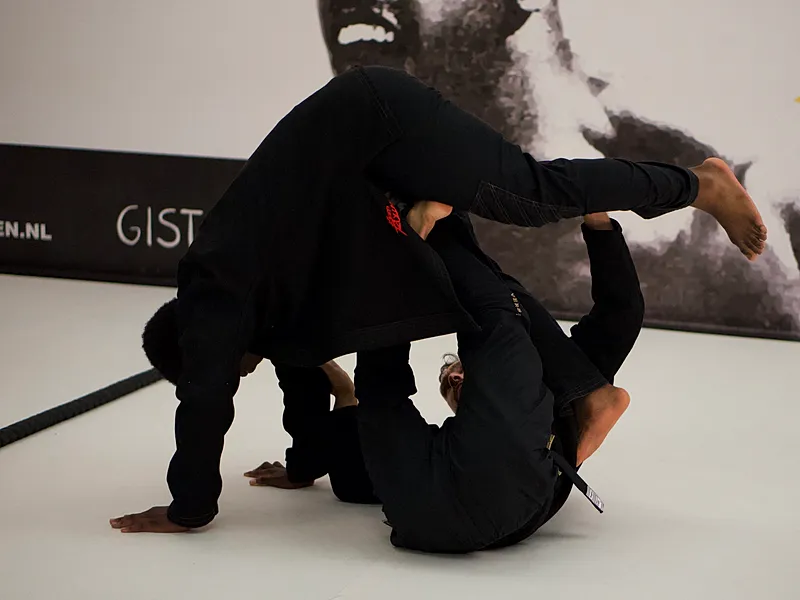 Twee BJJ-beoefenaars oefenen groundfighting technieken, waarbij een atleet in guard positie ligt terwijl de ander bovenop controleert.