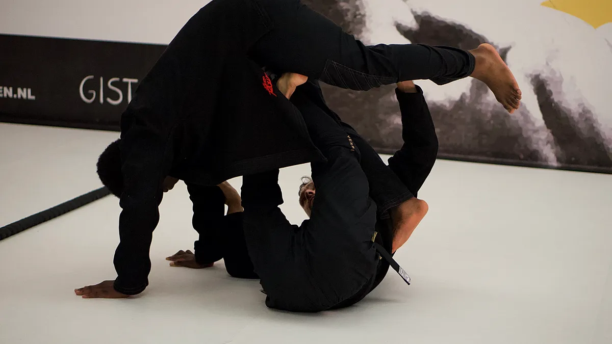 Twee BJJ-beoefenaars oefenen groundfighting technieken, waarbij een atleet in guard positie ligt terwijl de ander bovenop controleert.