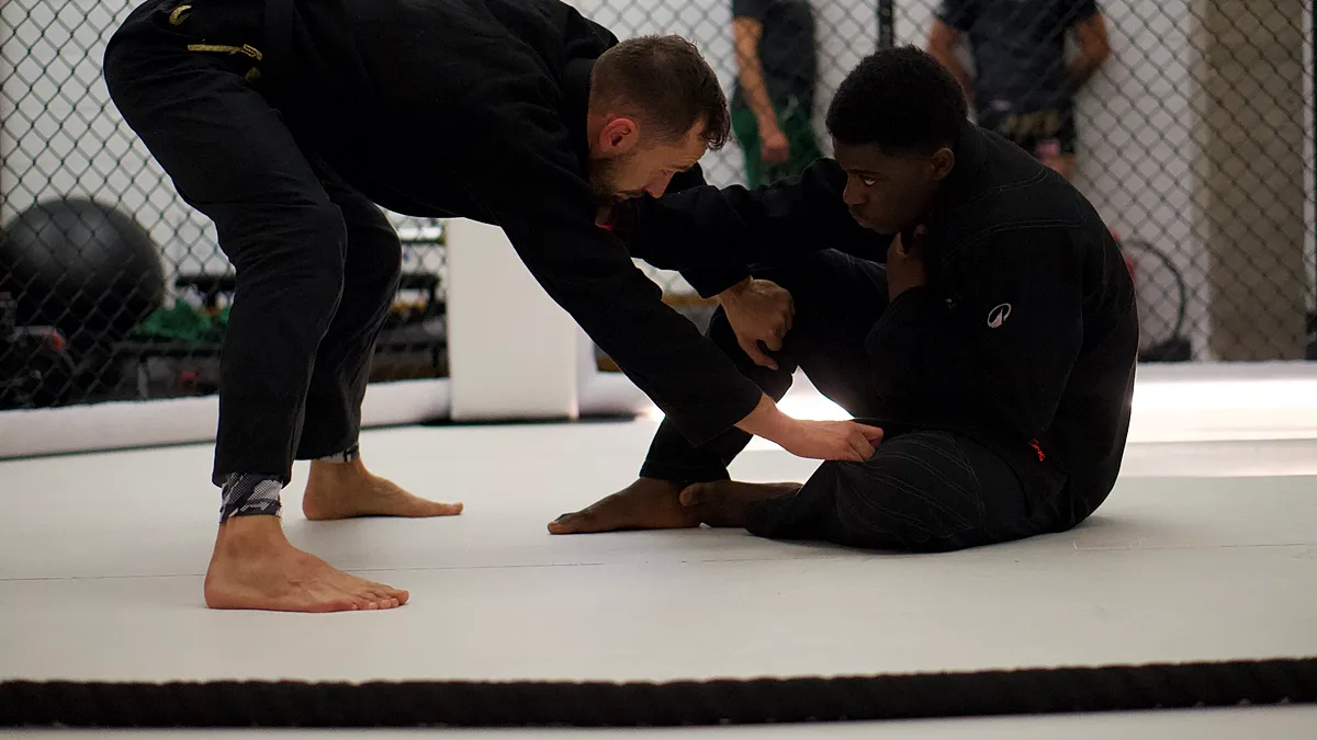 Een BJJ-instructeur demonstreert groundwork-technieken met een student in de guard positie op de matten.