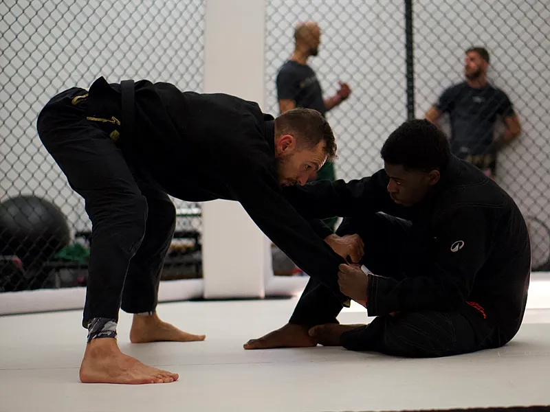 Een BJJ-instructeur demonstreert een guard-positie techniek met een student op de trainingsmat.