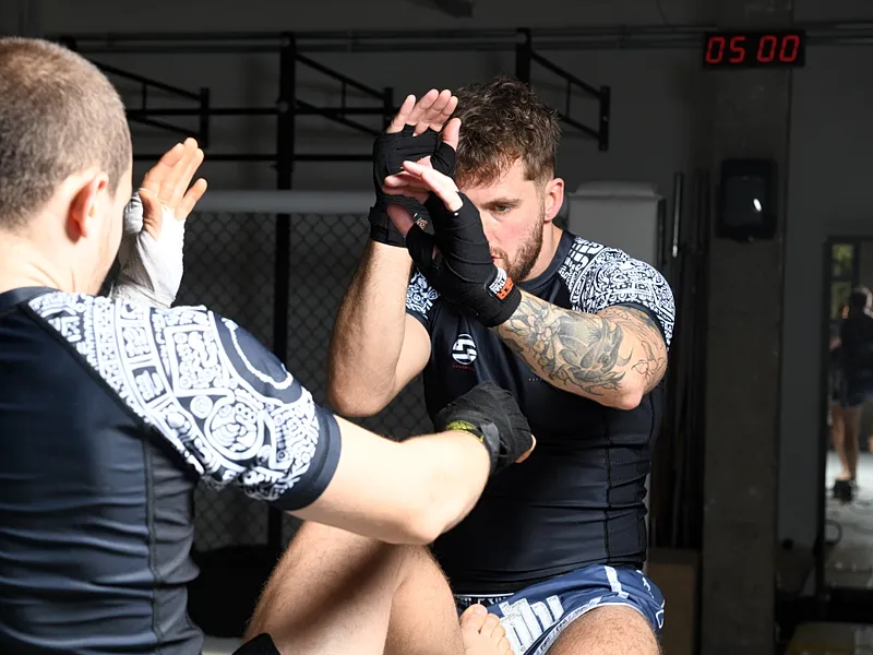 Twee MMA-fighters oefenen clinch- en slagtechnieken tijdens sparringsessie in een trainingshal.