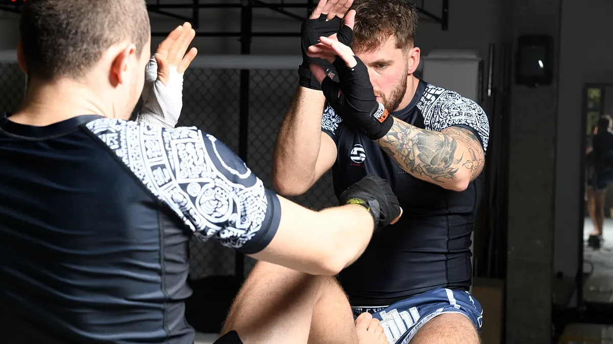Twee MMA-fighters oefenen clinch- en slagtechnieken tijdens sparringsessie in een trainingshal.