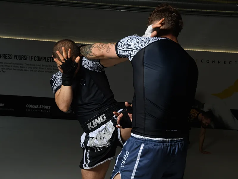 Twee BJJ-beoefenaars voeren intensieve grappling-sparring uit met clinch en kopcontrole tegen elkaar.
