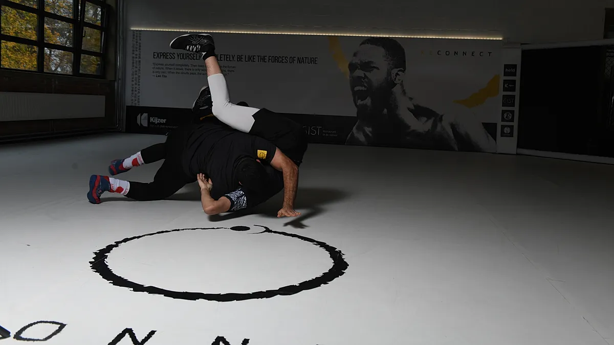 BJJ-beoefenaar in grondwerk positie tijdens trainingssessie in moderne sportfaciliteit.
